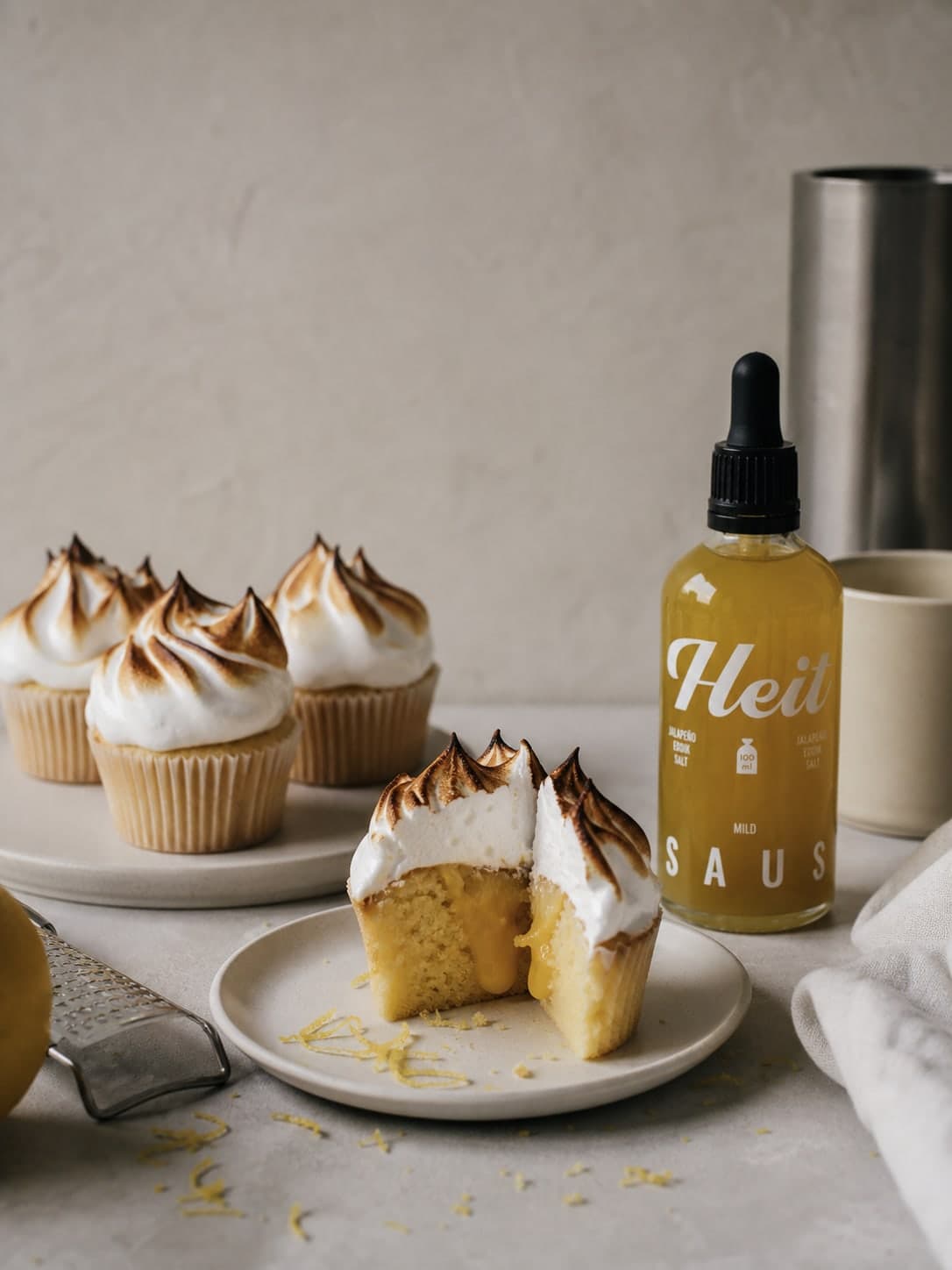 Lemon meringue cupcakes med brent marengs, én delt så sitronkremen vises, og en flaske Heit Mild