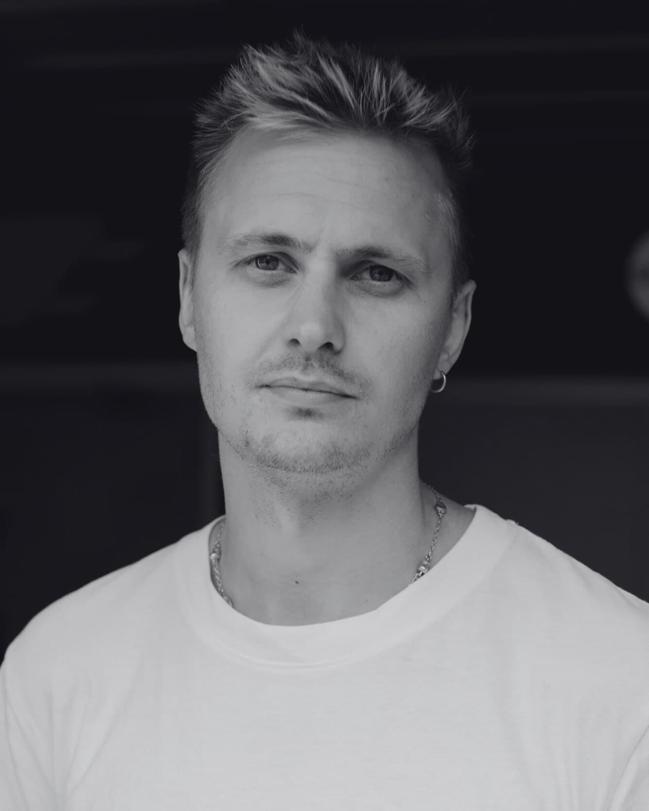 Christian Hovda Husan i hvit T-skjorte mot mørk bakgrunn, portrett i svart-hvitt
