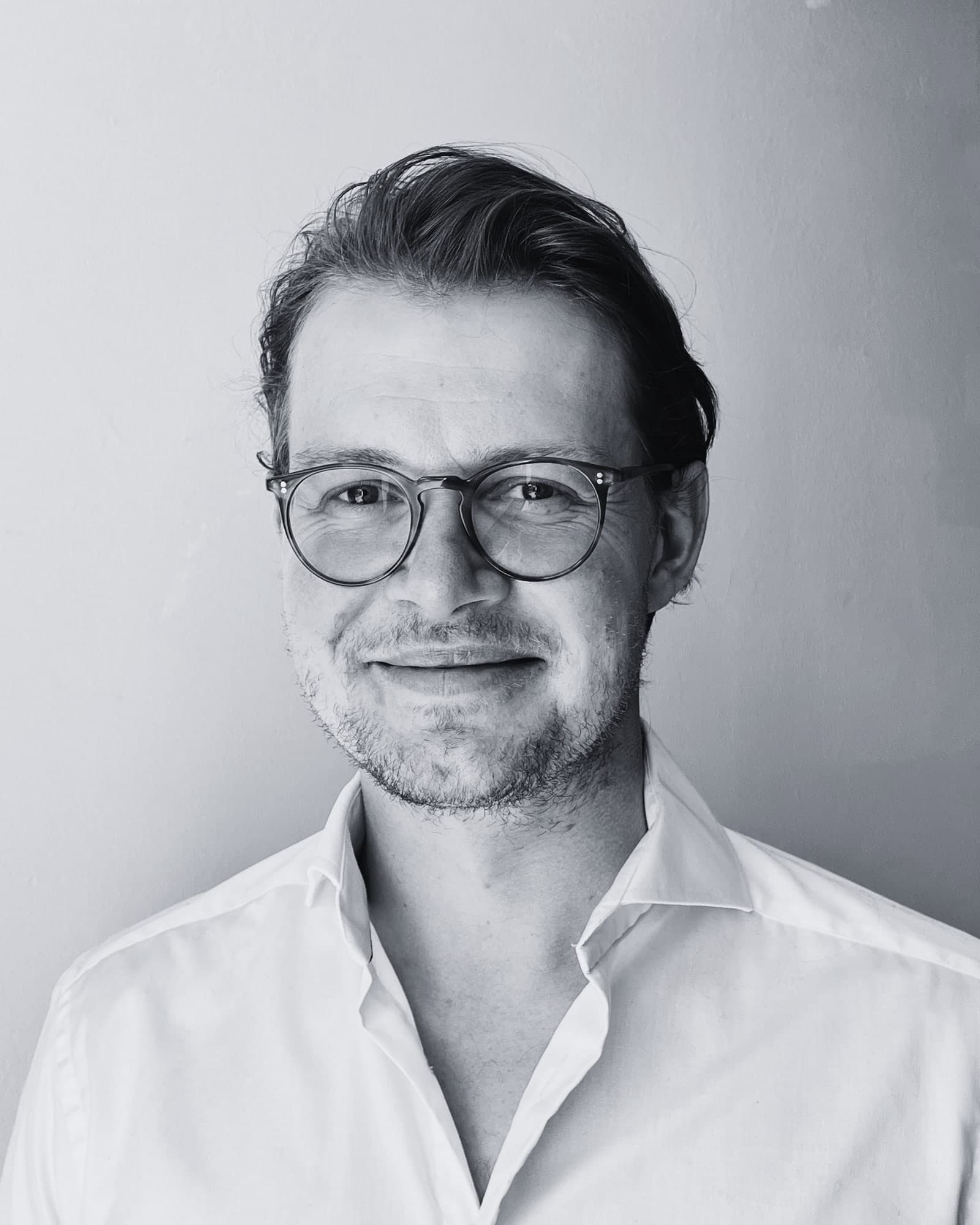 Truls Slettvoll med briller og hvit skjorte, smilende, portrett i svart-hvitt