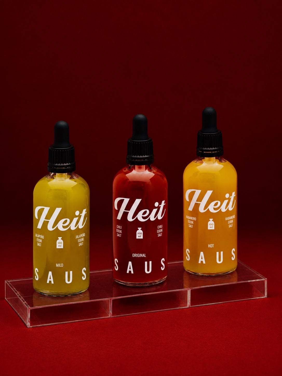 Heit Mild, Original og Hot saus på et klart akrylbrett mot dyp rød bakgrunn